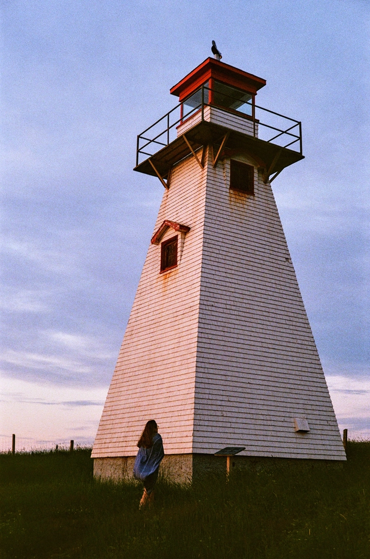 A picture of a girl looking up at a lighthouse