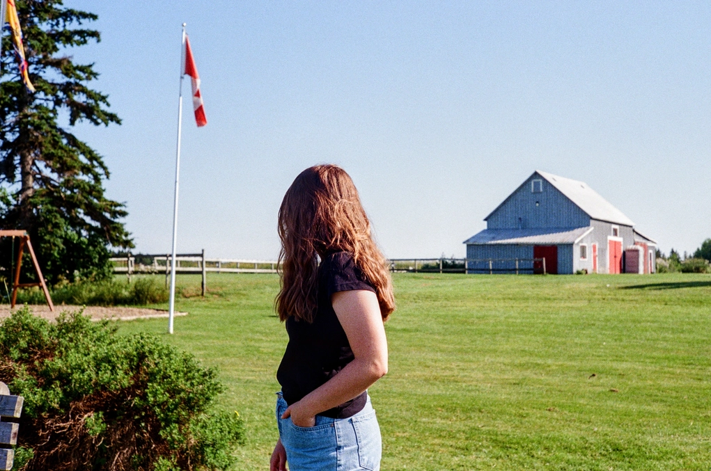 A picture of a girl in a field, barn in the distance