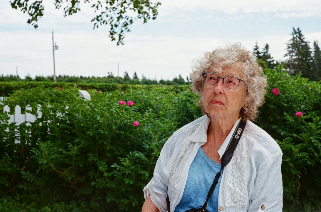 A picture of an older woman with bushes in the background